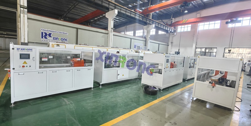 Multiple white PE pipe making machines by RSXinRong in industrial plant with operation panel and safety signs.jpg